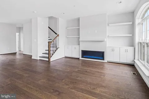 an empty room with wooden floor staircase and windows