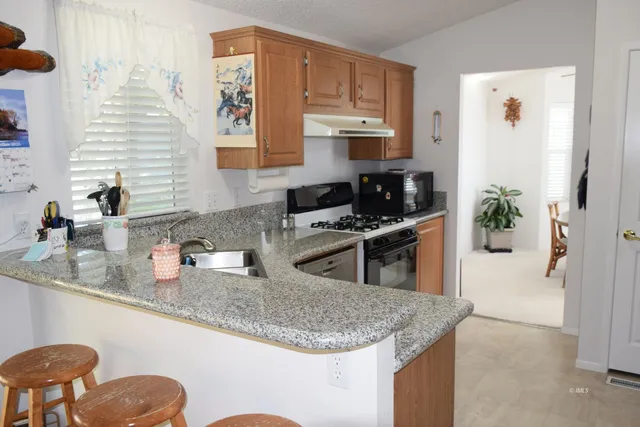 a kitchen with stainless steel appliances granite countertop a sink a stove and a wooden cabinets