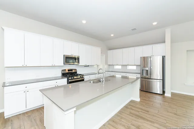 a kitchen with a refrigerator a stove a sink and white cabinets with wooden floor