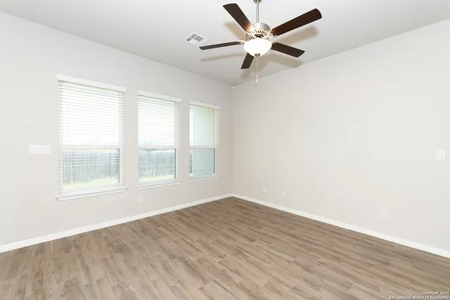 an empty room with wooden floor fan and windows
