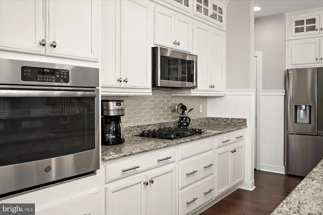 a kitchen with stainless steel appliances kitchen island granite countertop a stove a sink a refrigerator and white cabinets with wooden floor