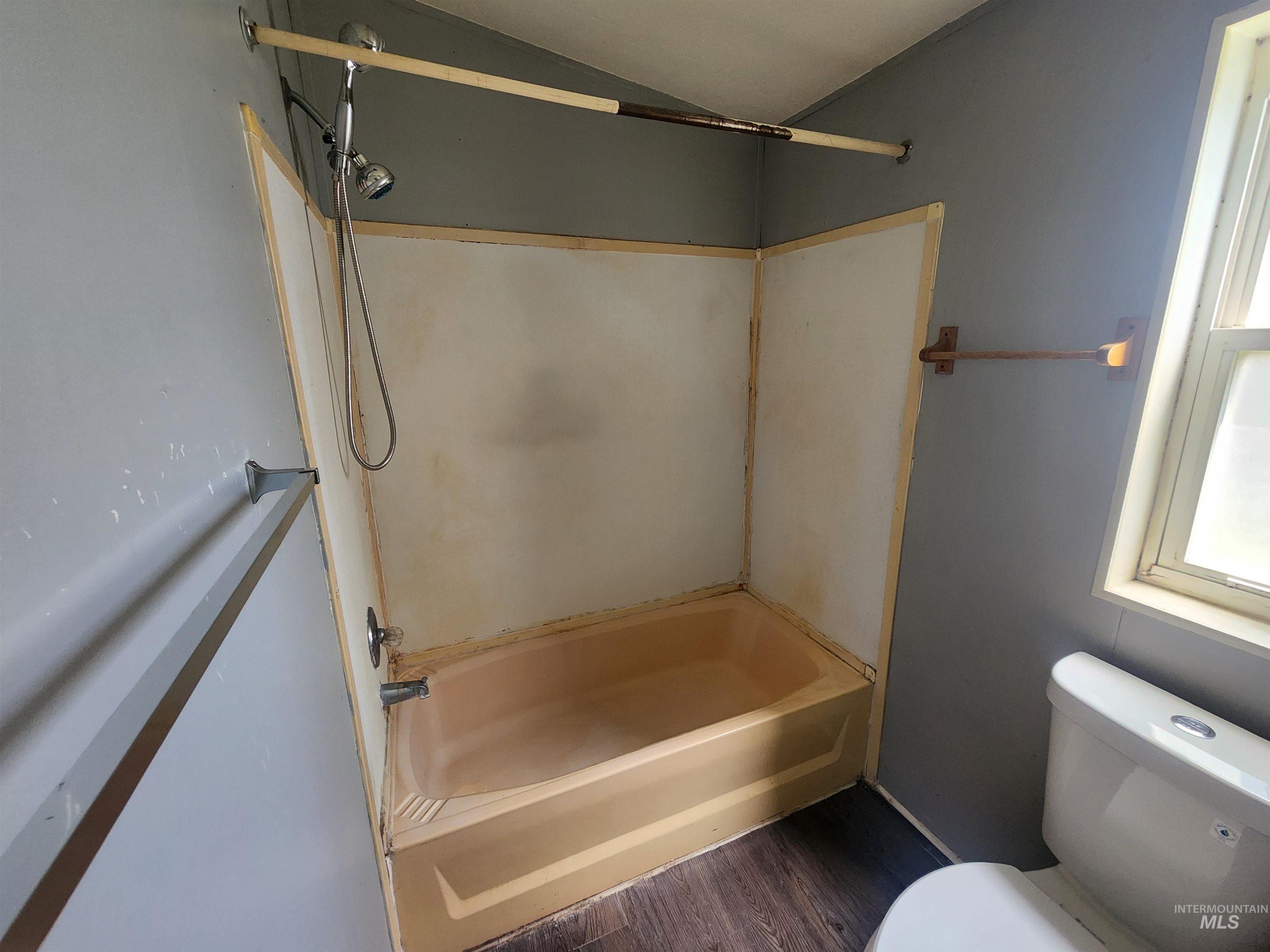 616 North Kings Road Nampa, ID 83687 - Photo 6 of 12 Bathroom featuring a built-in tub with a shower fixture, wood-finish flooring, a window, and a toilet