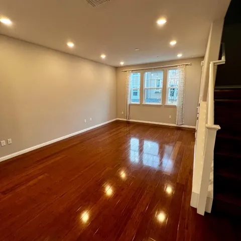 a view of an empty room with wooden floor and fan