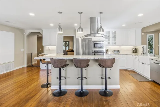 a kitchen with stainless steel appliances granite countertop a stove a sink dishwasher and white cabinets with wooden floor