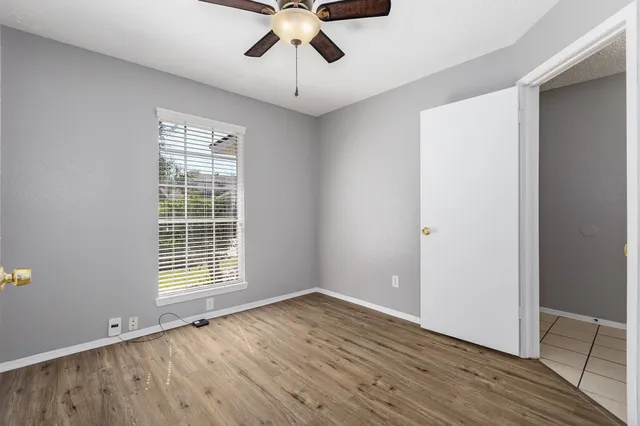 an empty room with wooden floor chandelier fan and windows