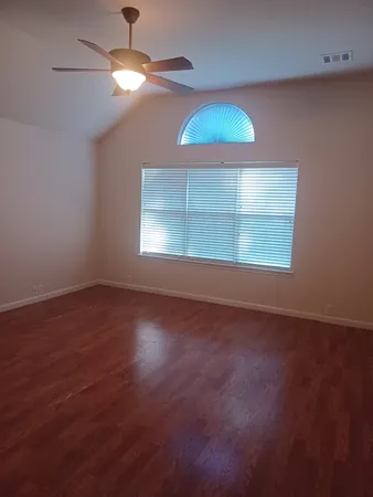 an empty room with wooden floor chandelier fan and windows