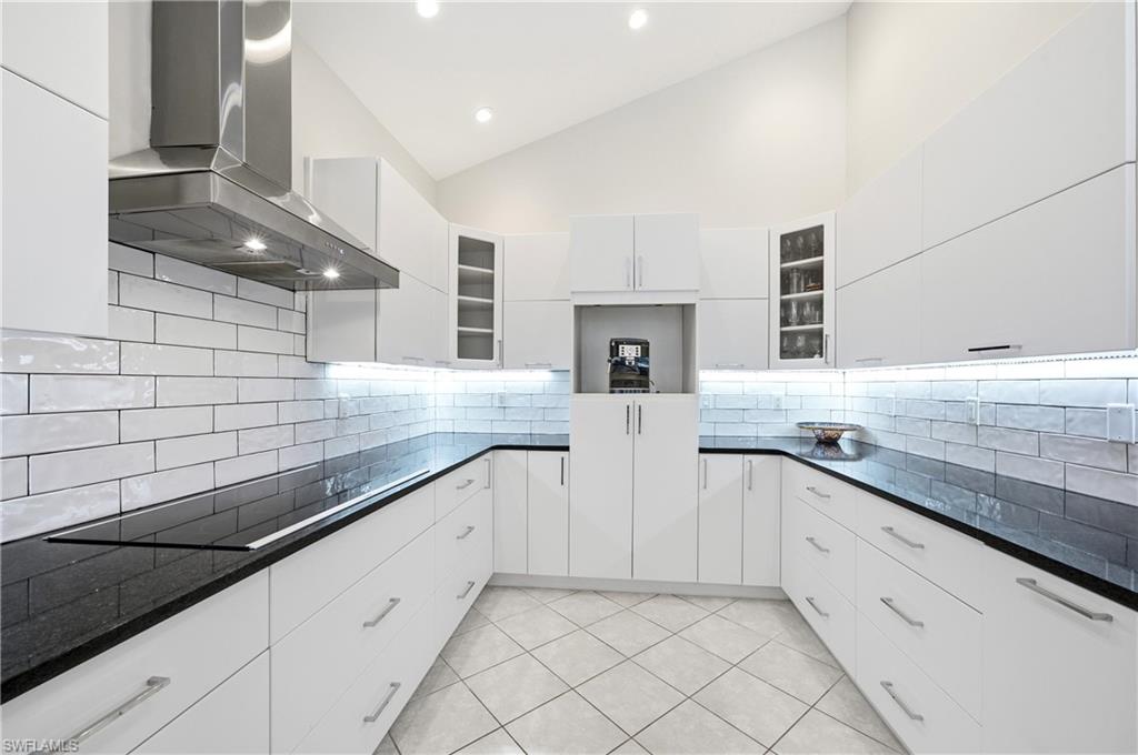 1960 Timarron Way Naples, FL 34109 - Photo 15 of 45 Bright kitchen featuring vaulted ceilings, white cabinetry, dark countertops, white subway tile backsplash, and under-cabinet lighting