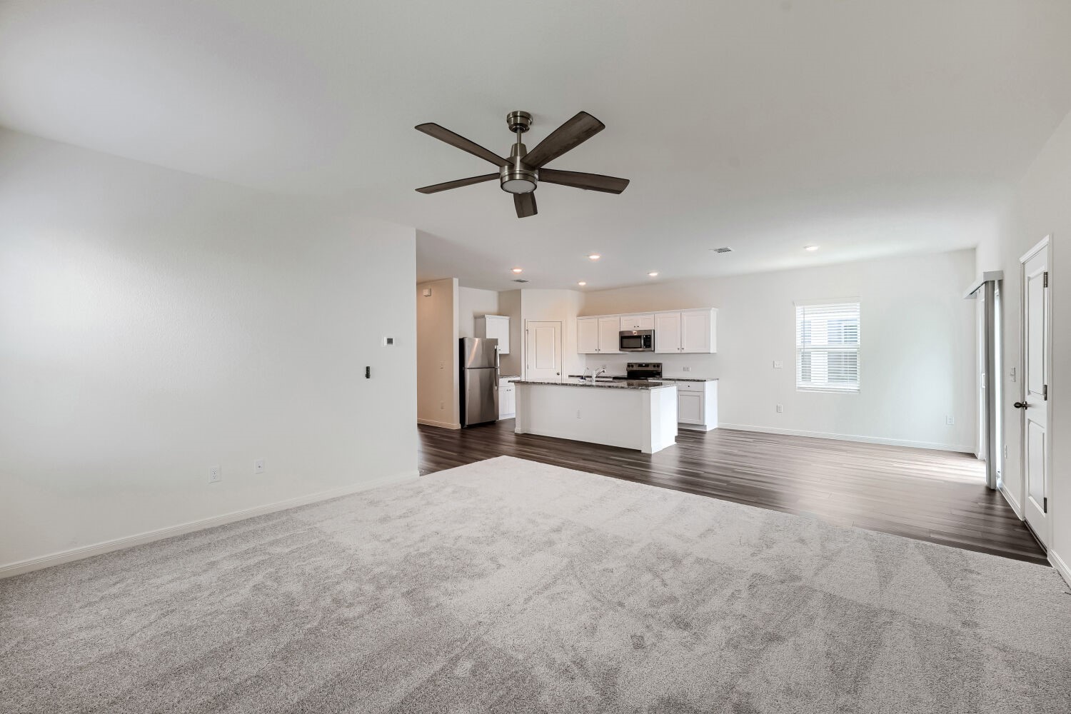 124 Mullen Way Taylor, TX 76574 - Photo 7 of 22 Open-concept living area featuring a modern ceiling fan, gray carpet, and wood-finish flooring