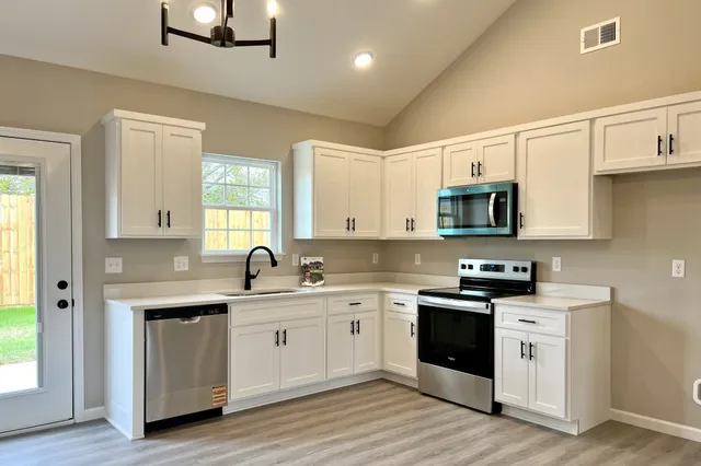 a kitchen with stainless steel appliances granite countertop white cabinets a sink dishwasher a stove and a refrigerator