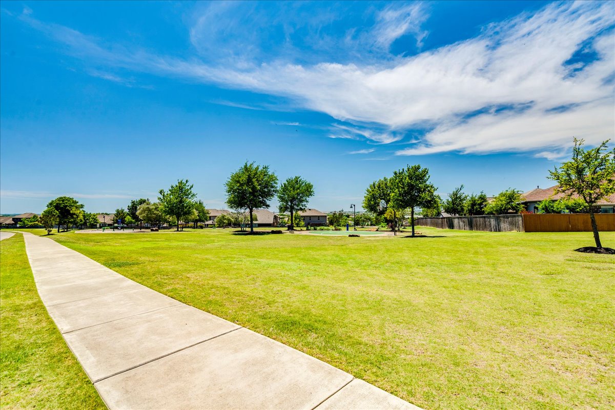 358 Jasper Trail Buda, TX 78610 - Photo 35 of 35 Expansive green space featuring a concrete pathway, mature trees, and a basketball court
