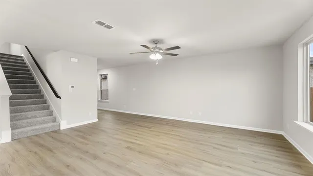 a view of an empty room with wooden floor and a ceiling fan