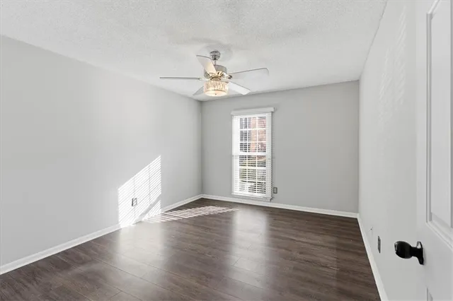 an empty room with wooden floor chandelier fan and windows