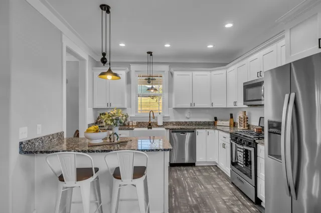 a kitchen with stainless steel appliances granite countertop a sink a stove a refrigerator and island with wooden floor