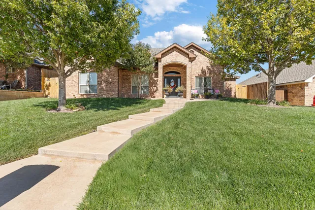 a view of a white house with a small yard plants and a large tree