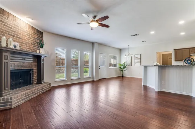 an empty room with wooden floor a ceiling fan a fireplace and windows