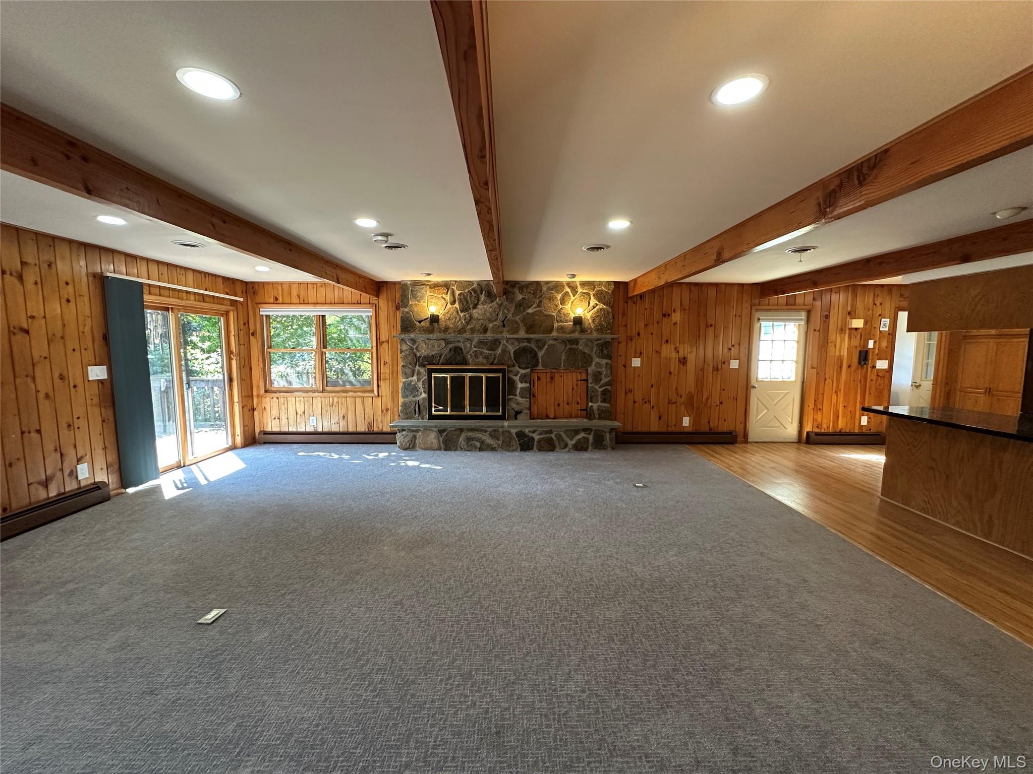 250 Rockland Road Roscoe, NY 12776 - Photo 13 of 32 Unfurnished living room with beamed ceiling, wooden walls, a stone fireplace, carpet, and recessed lighting