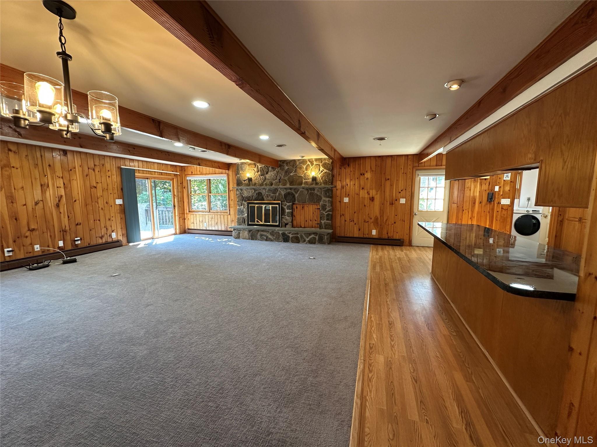 250 Rockland Road Roscoe, NY 12776 - Photo 14 of 32 Unfurnished living room featuring beam ceiling, wood walls, healthy amount of natural light, washer / dryer, and a stone fireplace