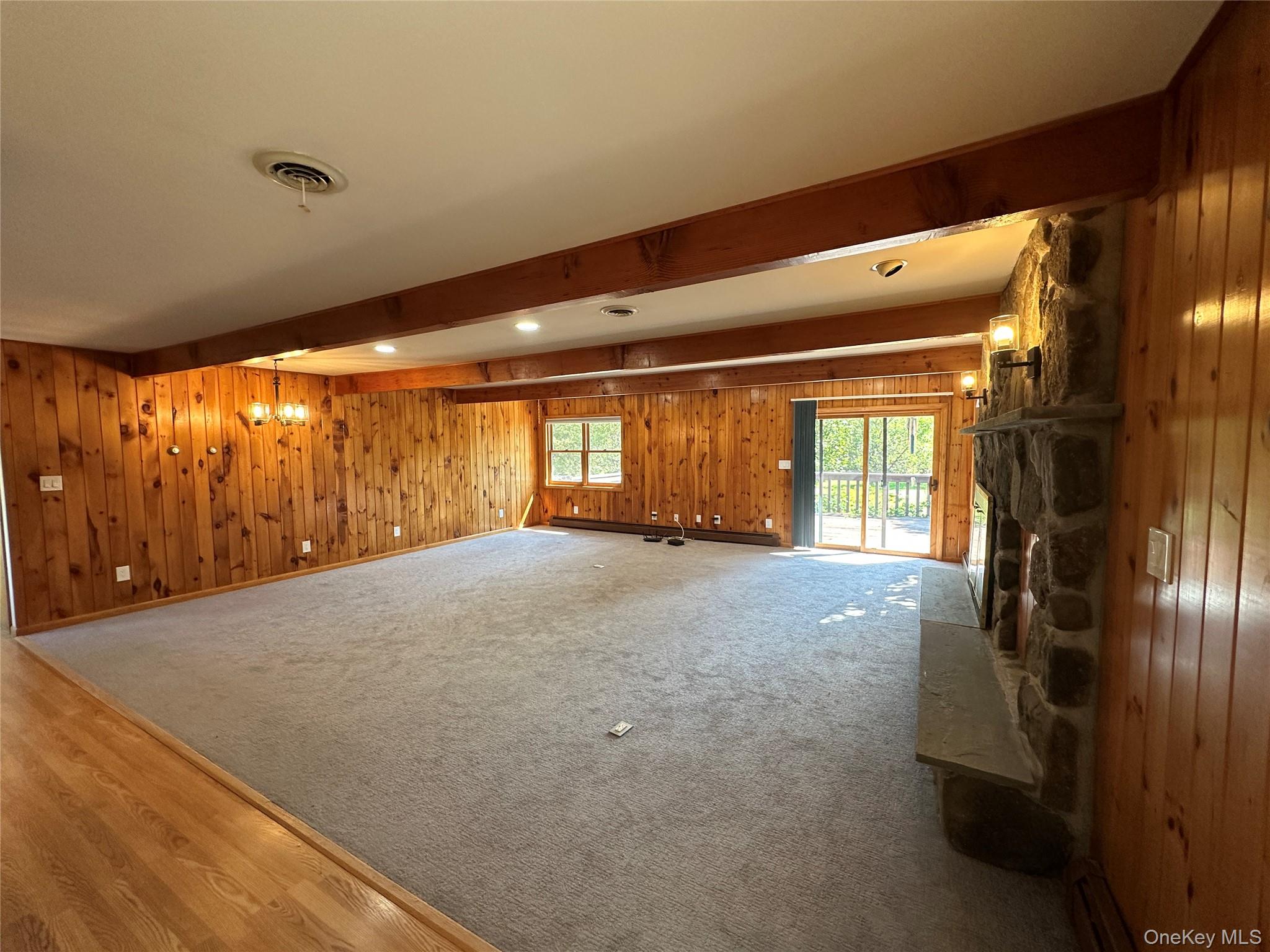 250 Rockland Road Roscoe, NY 12776 - Photo 17 of 32 Unfurnished living room featuring beam ceiling, a stone fireplace, healthy amount of natural light, wood finished floors, and wood walls