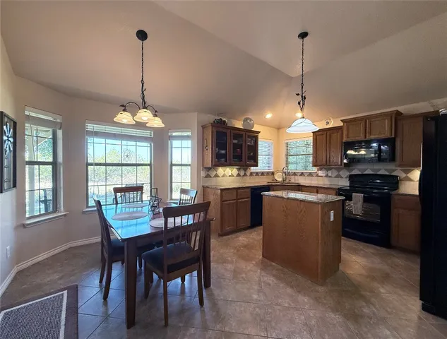 a kitchen with stainless steel appliances granite countertop a refrigerator a stove a kitchen island a dining table and chairs