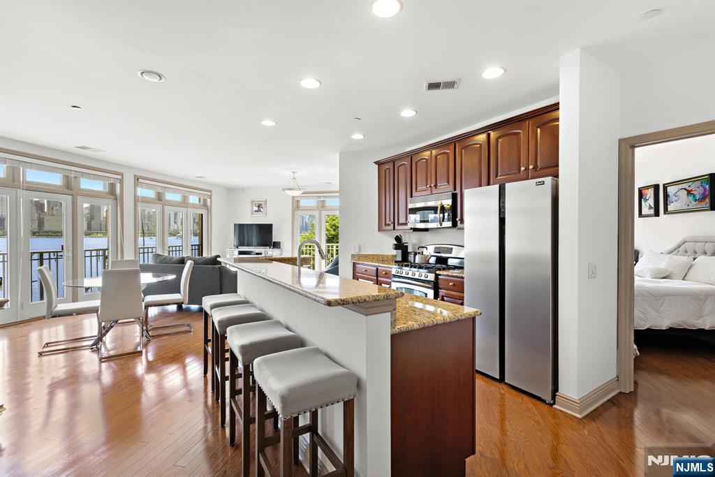 7400 River Road, Unit 208 North Bergen, NJ 07047 - Photo 5 of 18 a kitchen with stainless steel appliances a refrigerator a stove a dining table and chairs with wooden floor
