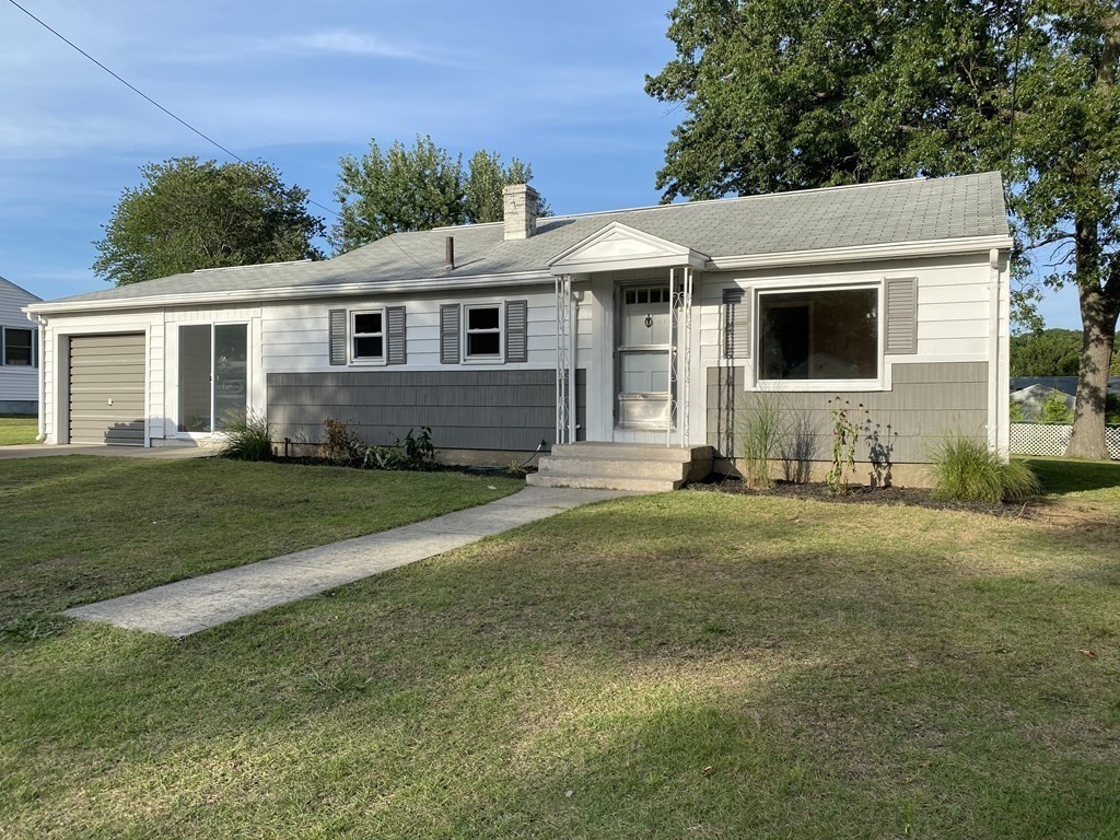 a view of a yard in front of a house with plants and large tree