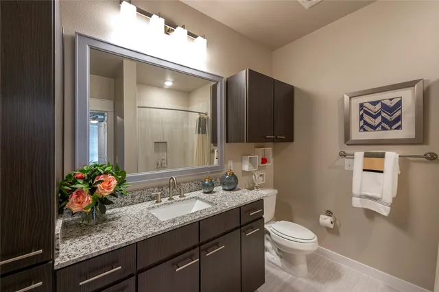 a bathroom with a granite countertop sink a large mirror a toilet and a shower