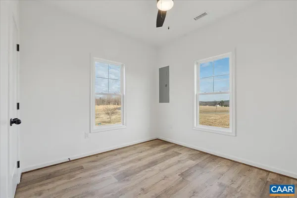 an empty room with wooden floor windows and fan