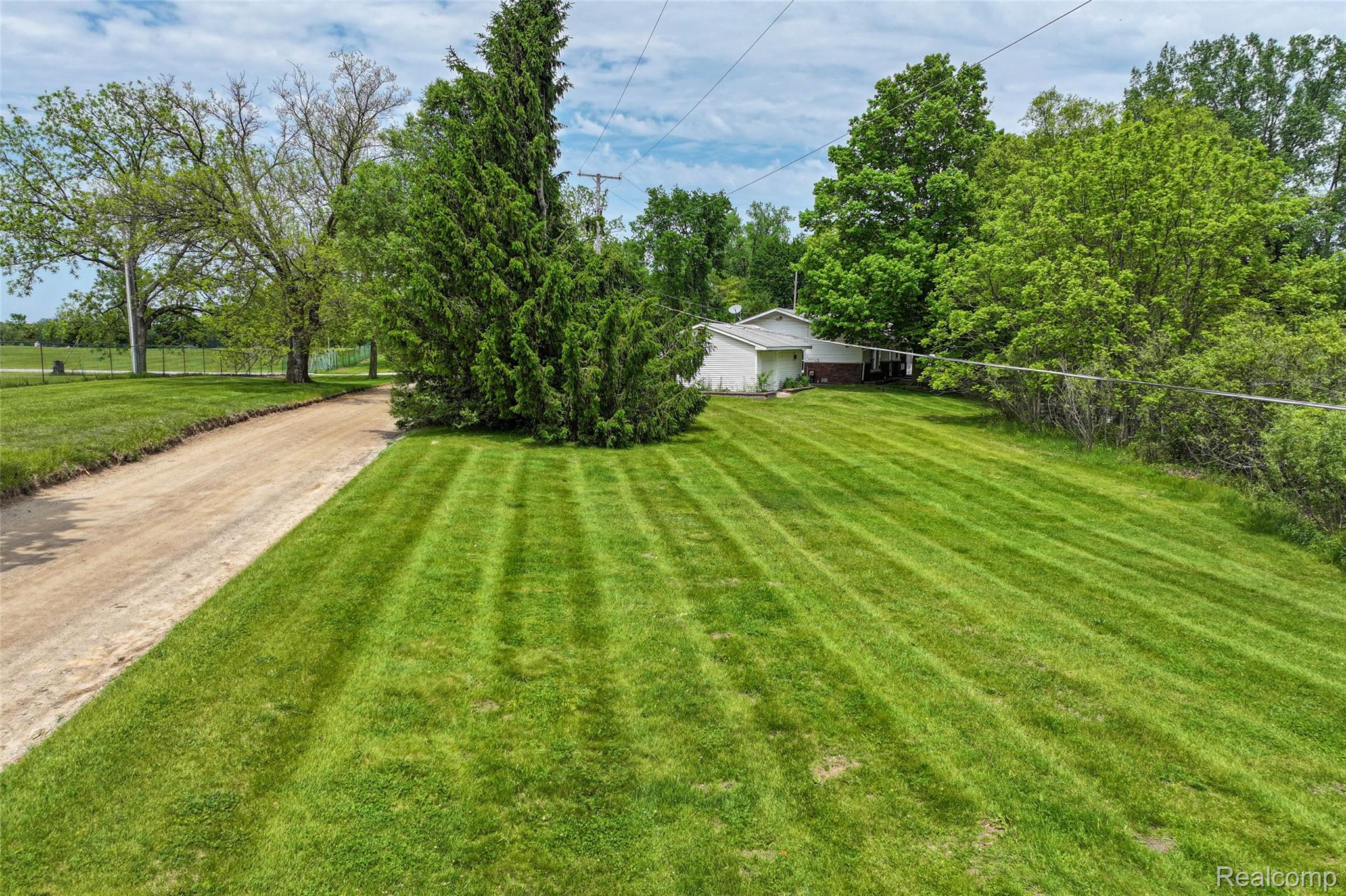 422 East Road Holly, MI 48442 - Photo 42 of 51 Expansive green lawn with striped mowing pattern, bordered by a dirt driveway and mature trees