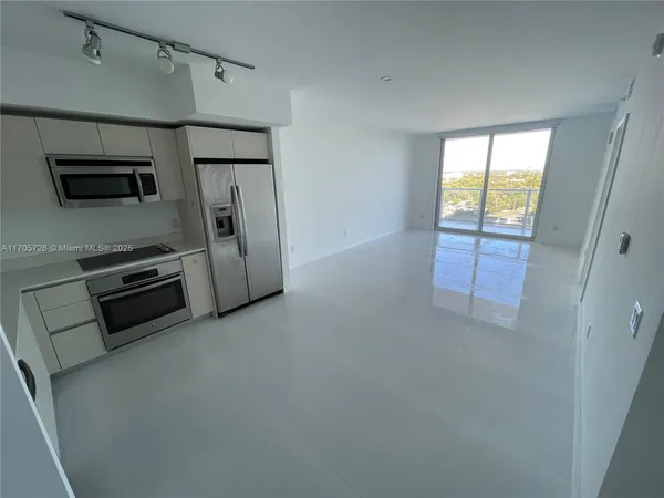 a view of a refrigerator in kitchen and an empty room