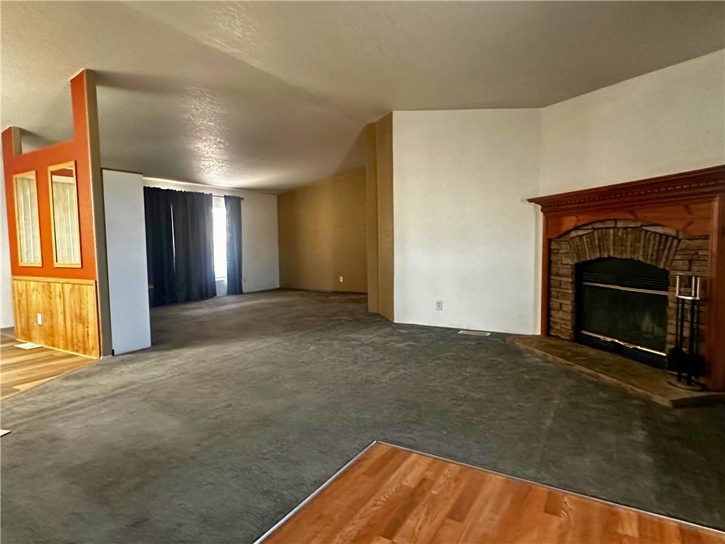 3746 Bouse Road Golden Valley, AZ 86413 - Photo 3 of 53 Unfurnished living room featuring wood finished floors, a brick fireplace, carpet, and a textured ceiling