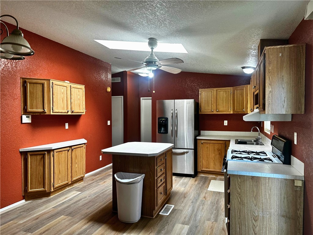 3746 Bouse Road Golden Valley, AZ 86413 - Photo 9 of 53 Kitchen featuring vaulted ceiling, a skylight, range with gas cooktop, a textured wall, and stainless steel refrigerator with ice dispenser