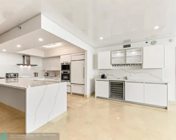 a large white kitchen with stainless steel appliances granite countertop a stove and a sink
