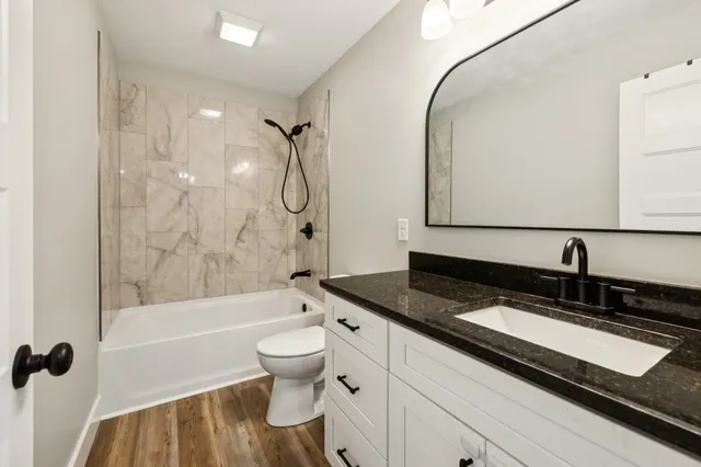 a bathroom with a granite countertop sink a toilet a mirror a bathtub and shower