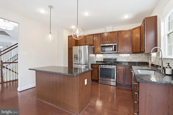 a kitchen with stainless steel appliances granite countertop a refrigerator a sink a stove a microwave and wooden floors