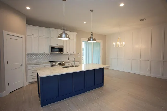 a kitchen with stainless steel appliances granite countertop a sink a stove a refrigerator and white cabinets with wooden floor