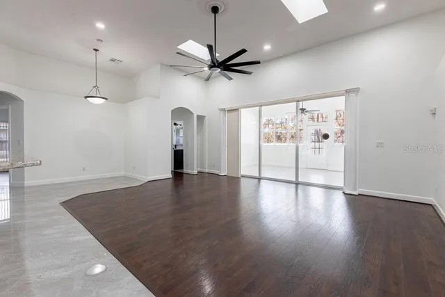 an empty room with wooden floor ceiling fan and windows