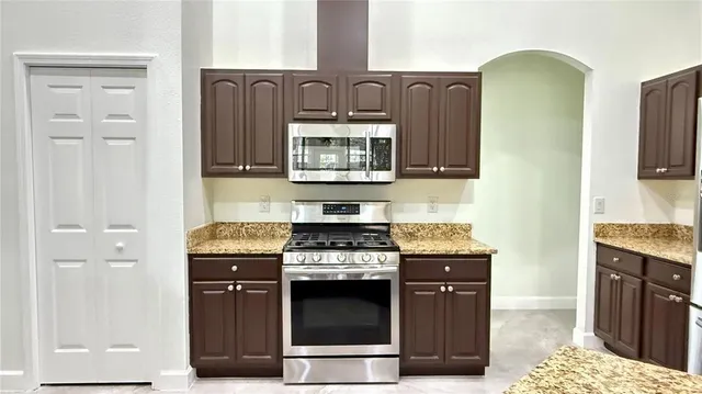 a kitchen with granite countertop a stove a microwave and wooden cabinets