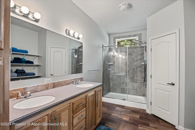 a bathroom with a granite countertop double vanity sink a mirror and a shower