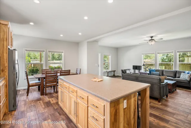 a view of a kitchen with kitchen island a stove a refrigerator a dining table and chairs with wooden floor