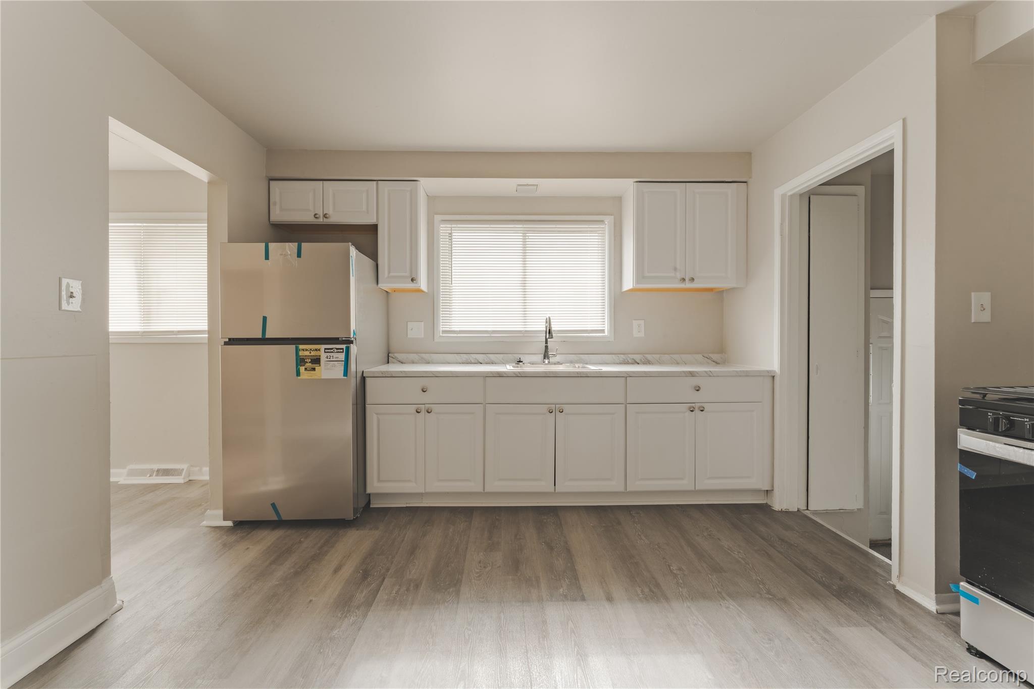 93 West Princeton Avenue Pontiac, MI 48340 - Photo 21 of 31 Kitchen featuring wood-finish flooring, white cabinetry, a double basin sink, and a stainless steel refrigerator