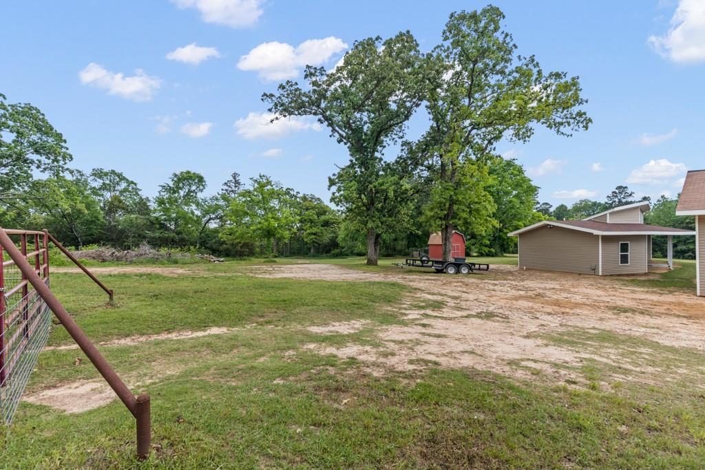 1129 Holly Road Gilmer, TX 75644 - Photo 29 of 31 Expansive outdoor area featuring a metal fence, mature trees, and a detached structure with light brown siding and a covered porch
