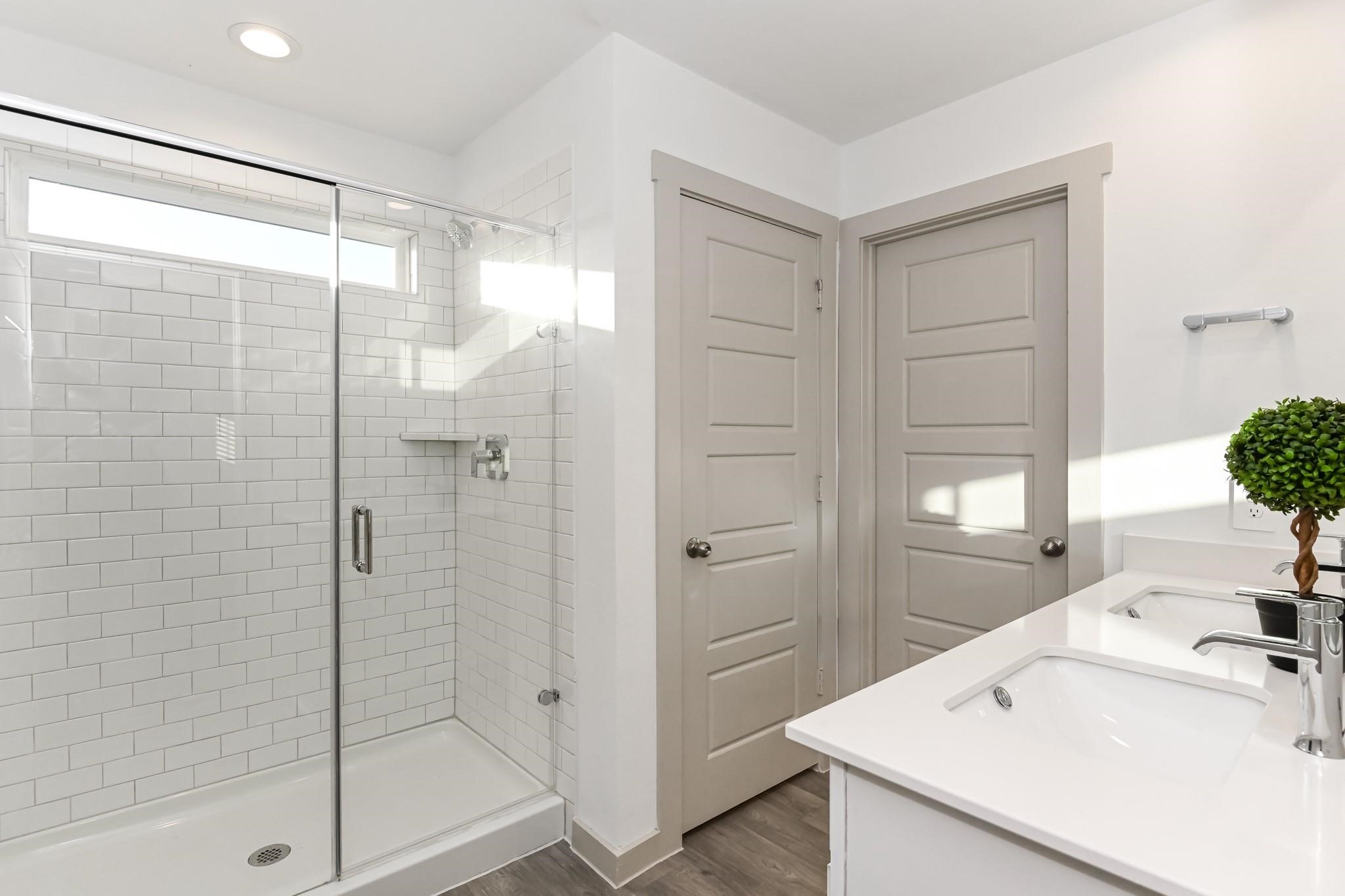7811 Golden Rubia Lane Rosharon, TX 77583 - Photo 8 of 10 Modern bathroom featuring a glass-enclosed shower with white subway tiles, dual sinks with sleek faucets, and neutral-colored doors. Bright and inviting space with contemporary fixtures.