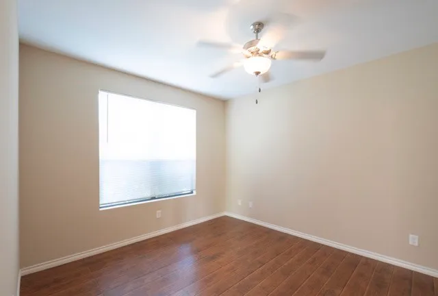 an empty room with wooden floor chandelier fan and windows