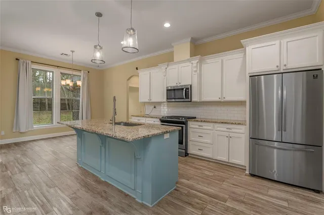 a kitchen with kitchen island granite countertop a stove a sink a refrigerator and white cabinets with wooden floor