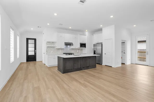 a large white kitchen with kitchen island a sink wooden floor and a refrigerator