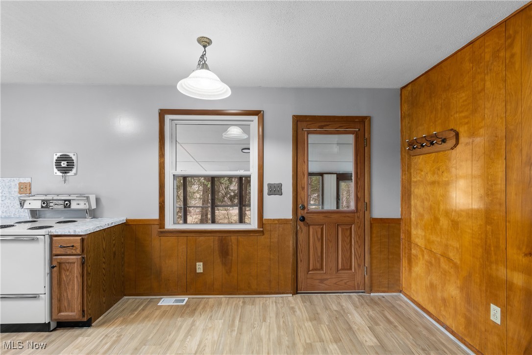 Kitchen featuring wooden walls, visible vents, a wainscoted wall, brown cabinets, and electric range