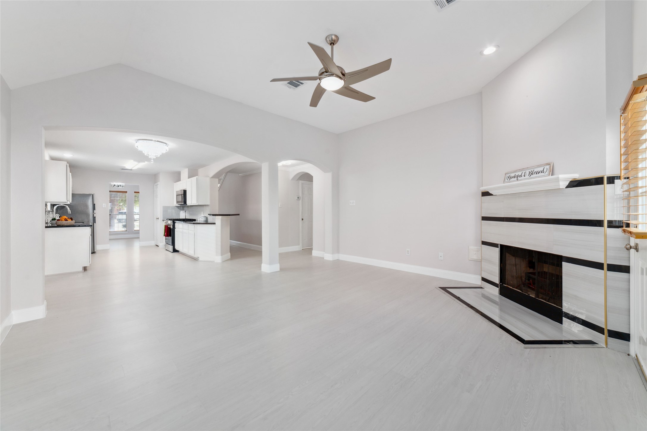 8330 Malin Court Houston, TX 77083 - Photo 6 of 21 This photo showcases a bright, open-concept living area with light and a modern ceiling fan. It features a sleek, contemporary fireplace and an adjacent kitchen with stainless steel appliances and white cabinetry. The space is well-lit, creating a welcoming atmosphere.