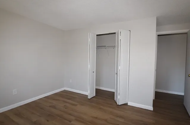a view of an empty room with wooden floor and closet