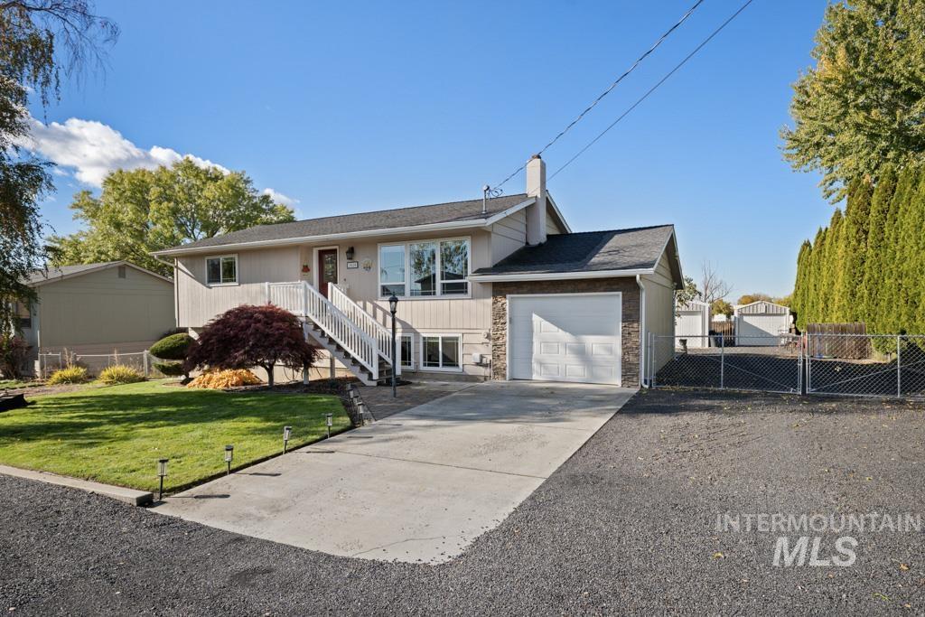 View of front of property featuring driveway, an attached garage, a chimney, stone siding, and stairway