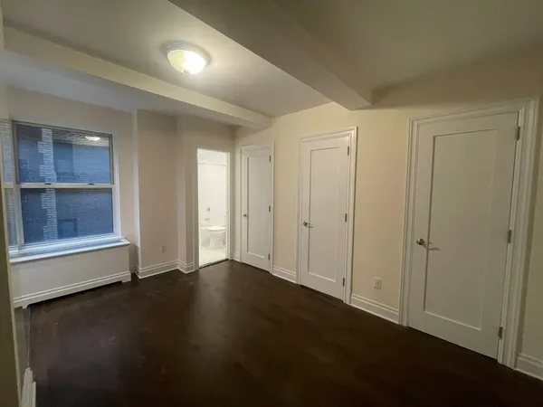 an empty room with wooden floor cabinet and windows